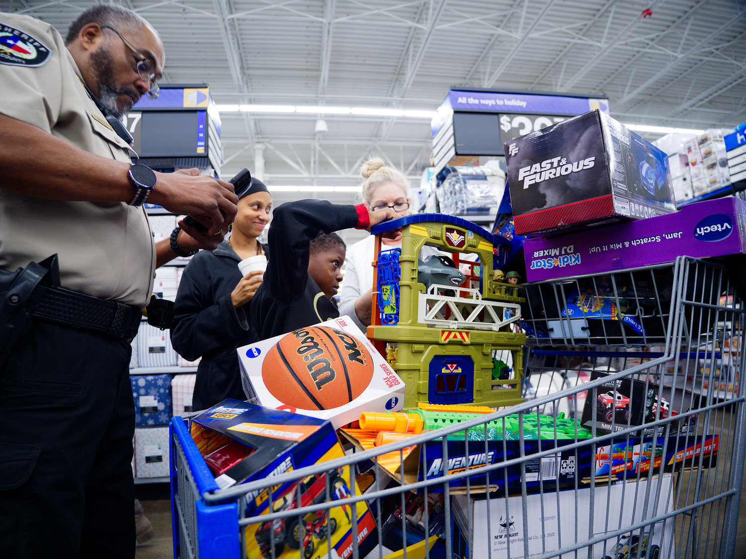 Wood County Sheriff’s Dept. Deputy AG Sessions tallies toys for Gavin Fields during last Tuesday’s annual Blue Santa event at Walmart in Mineola. Area law enforcement officers were paired with 52 children for a $300 Christmas shopping spree. See Page 10A for story, more photos.